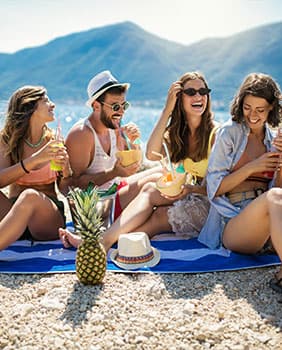 Freunde die am Strand auf einem Handtuch sitzen